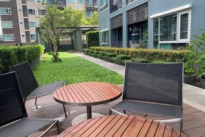 An outdoor seating area with a round wooden table and two chairs, surrounded by a well-maintained hedge and a small tree. - Thailand Pattaya Center Sea Seascape Apartment (Pattaya)