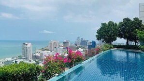 Ein Rooftop-Endlospool mit Blick auf die Stadt, umgeben von Grünpflanzen und rosa Blumen.
