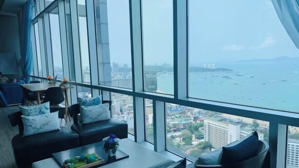 Ein modernes Wohnzimmer mit großen Fenstern, einer Sofagarnitur, einem Couchtisch und Blick auf das Meer und die Skyline.