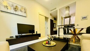 A modern living room with a flat-screen TV, dark coffee table, and a dining area with a glass table and chairs. - CEMELDA (Budva)