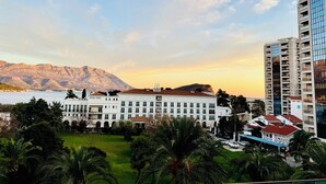A hotel with a white facade, multiple balconies, and a view of mountains in the background. - CEMELDA (Budva)
