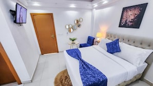 Habitación de hotel con una cama grande, un televisor, una puerta, una mesita con una lámpara y un cuadro de un leopardo en la pared.