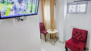 Una sala de estar con una televisión, una silla roja, una mesita redonda y un ventanal con rejas decorativas de hierro.