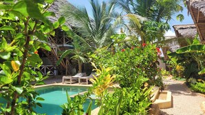 A pool surrounded by lush greenery and thatched-roof structures. - SuBanda Boutique Hotel (Makunduchi)