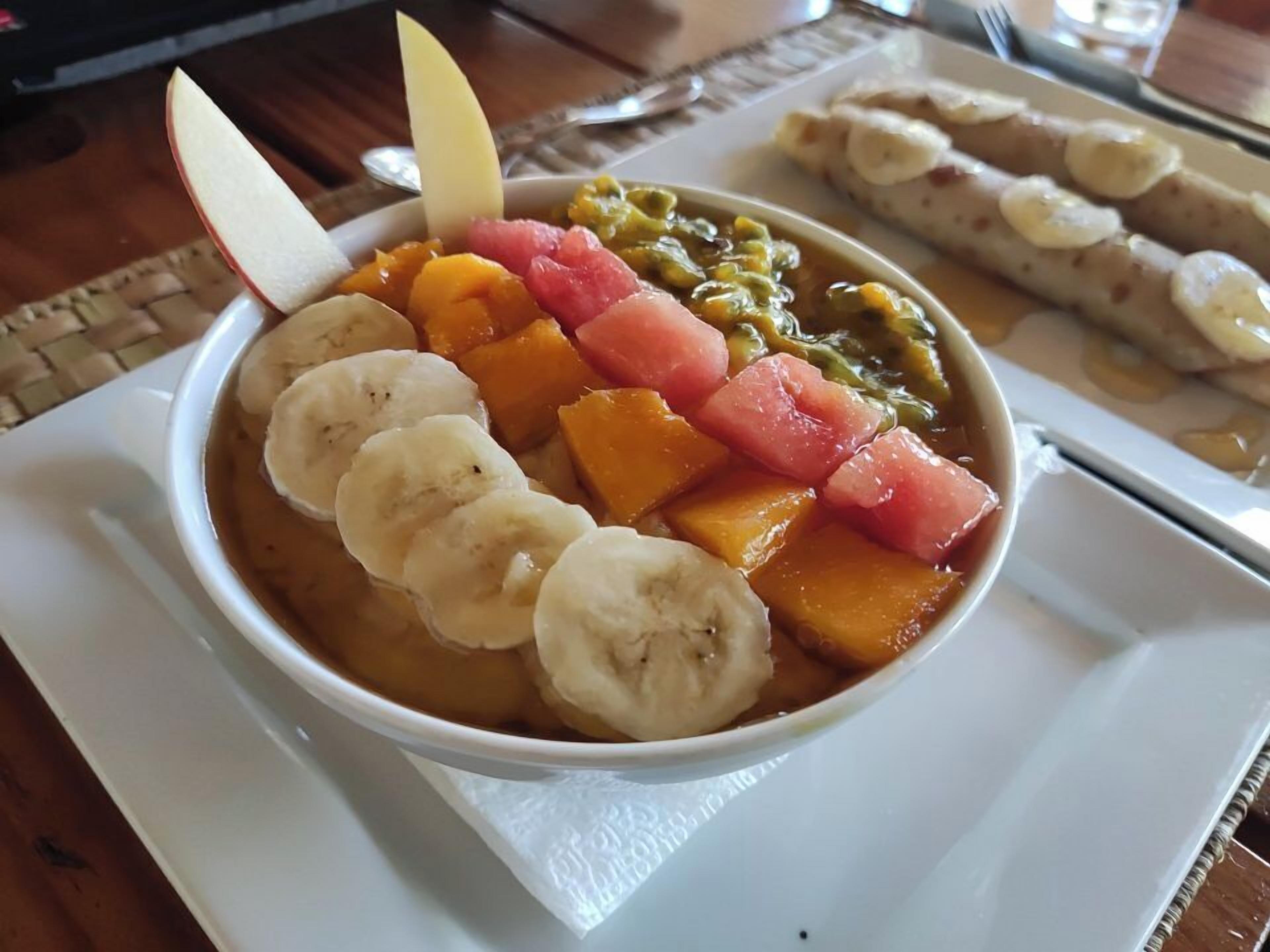 Un tazón de ensalada de frutas con plátanos, sandía y judías verdes sobre un plato blanco.