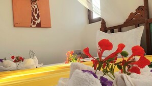 A neatly made bed with white towels and a bouquet of flowers, a painting of a giraffe on the wall, and a wooden headboard. - SuBanda Boutique Hotel (Makunduchi)