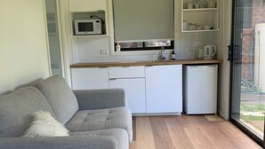 A modern kitchen with white cabinets, a microwave, and a coffee maker. There is a grey sofa with a white throw pillow in the living area. - Family Beach House. Pet friendly. 5 minute walk to the longest beach in Aus! (Woodside Beach)