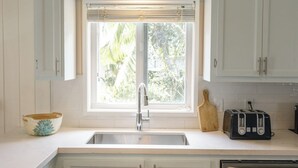 A kitchen with white cabinets, a stainless steel sink, a window with blinds, a wooden cutting board, and a toaster. - Charming Tickled Pink 2BR, 3BD, 3BTH home, minutes from pink sand beach (Harbour Island)