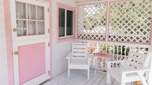 A white door with pink trim, a window with a lattice screen, and a white bench with a pink table. - Charming Tickled Pink 2BR, 3BD, 3BTH home, minutes from pink sand beach (Harbour Island)