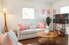 A living room with a sofa, a round coffee table, a TV, and a bookshelf. - Charming Tickled Pink 2BR, 3BD, 3BTH home, minutes from pink sand beach (Harbour Island)