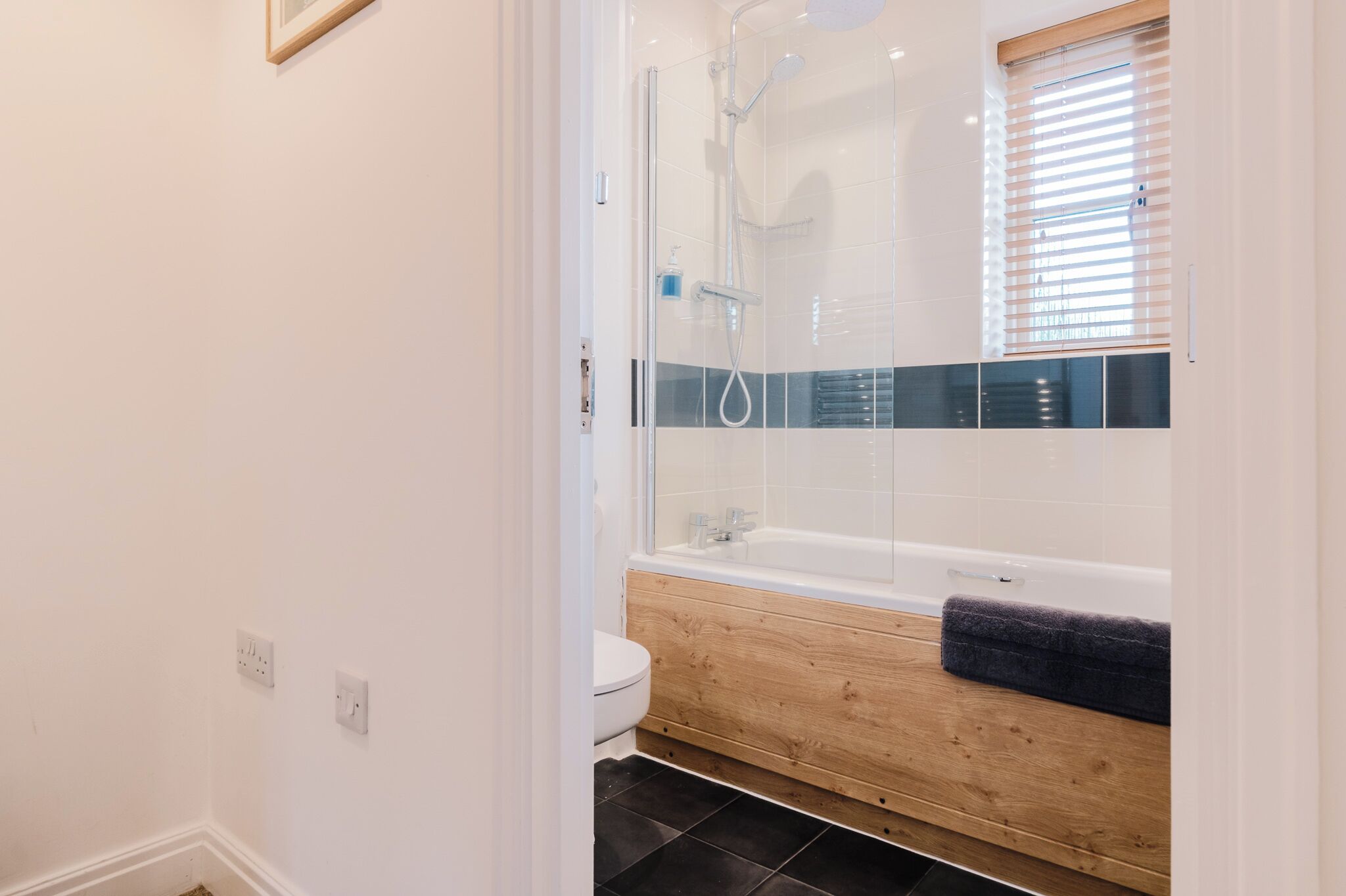 A modern bathroom with a glass-enclosed shower, a wooden bathtub, and a toilet.