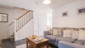 A living room with a staircase, a sofa, a coffee table, and a door. - Charming 2 Bedroom Home in the Cotswolds (Cheltenham)