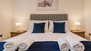 A neatly made bed with white and blue bedding, two bedside tables with lamps, and a framed picture of a fox on the wall. - Charming 2 Bedroom Home in the Cotswolds (Cheltenham)