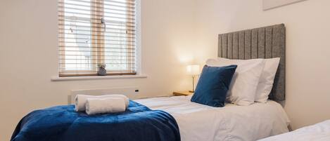 Une chambre d’hôtel avec deux lits, une fenêtre avec des stores, une lampe de chevet et une œuvre d’art accrochée au mur.