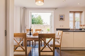 A dining area with a table set for four, a stone wall, and a window with blinds. - Charming 2 Bedroom Home in the Cotswolds (Cheltenham)