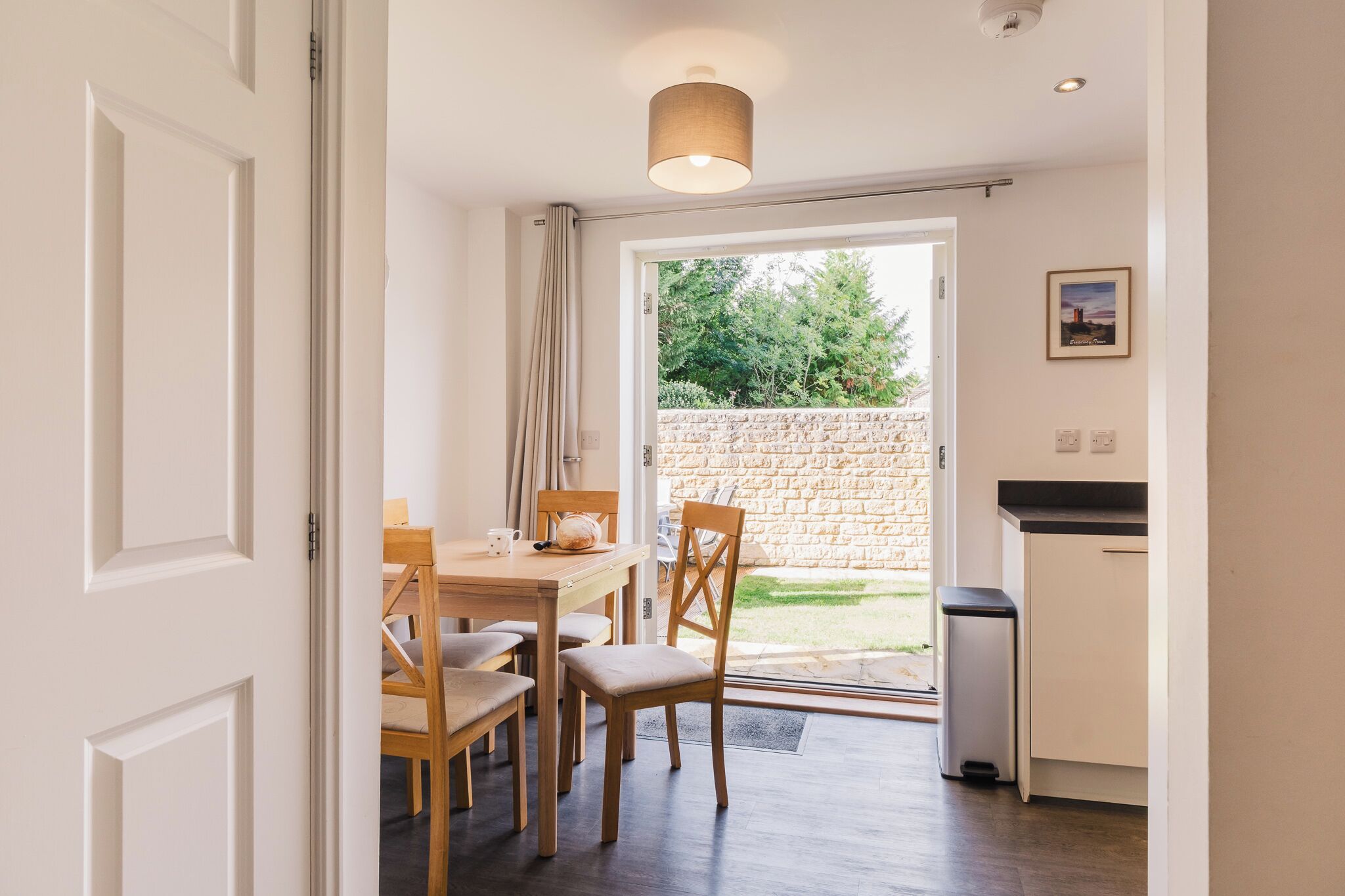 A dining area with a table, chairs, and a view of the garden through the door.