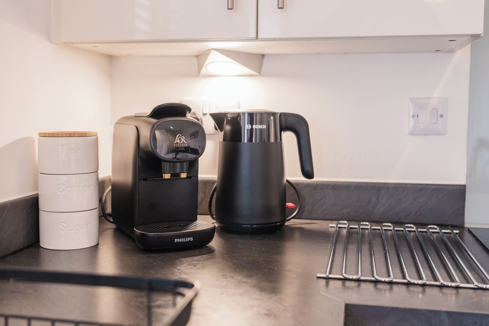 A kitchen counter with a coffee maker, a kettle, and a sugar container.