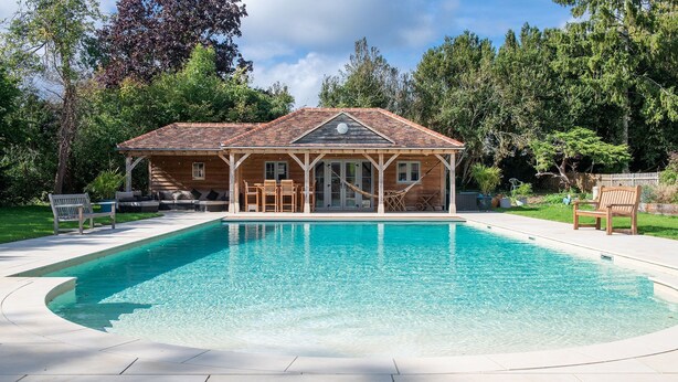 A wooden house with a swimming pool, surrounded by trees.