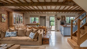A cozy living room with a sofa, a dining area, and a kitchen with wooden beams and blue cabinets.