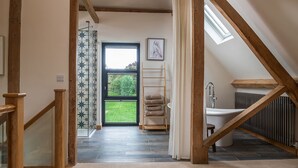 A modern bathroom with a bathtub, a shower, and a toilet. There is a window providing natural light and a view of the outdoors.