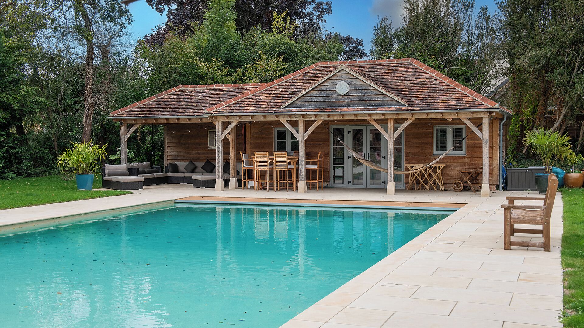 A wooden cabin with a pool, outdoor seating, and a covered patio area.