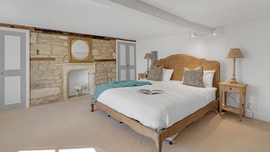 Ein Schlafzimmer mit Kamin aus Stein, einem Bett mit weißer Bettwäsche, einem hölzernen Kopfteil und einem Nachttisch mit Lampe.
