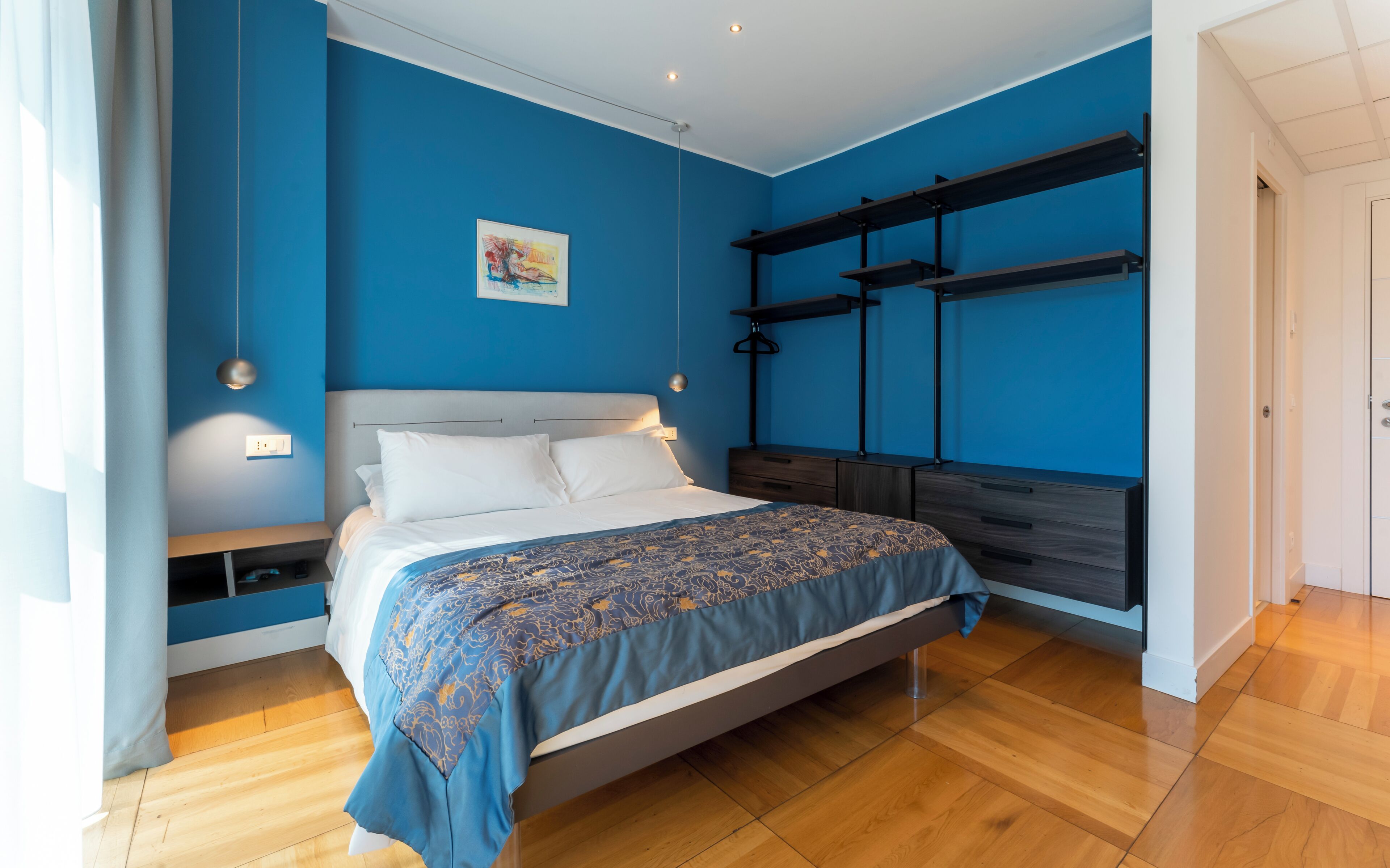 A bedroom with a bed, bedside table, and a wall-mounted shelf unit.