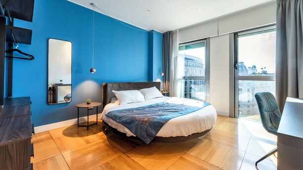 A modern hotel room with a large bed, a round desk, a chair, a small table with a plant, and a large window with a city view. - La Dimora di Missori (Milan)