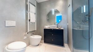 A modern bathroom with a white toilet, a white sink, a black vanity, a glass shower enclosure, and a large mirror. - La Dimora di Missori (Milan)