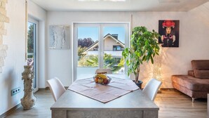 A modern interior with a dining table, chairs, a fruit bowl, a potted plant, a sofa, and a painting on the wall. - Apartment 'Fewo-wosink' with private terrace, balcony and Wi-Fi (Bad Krozingen)