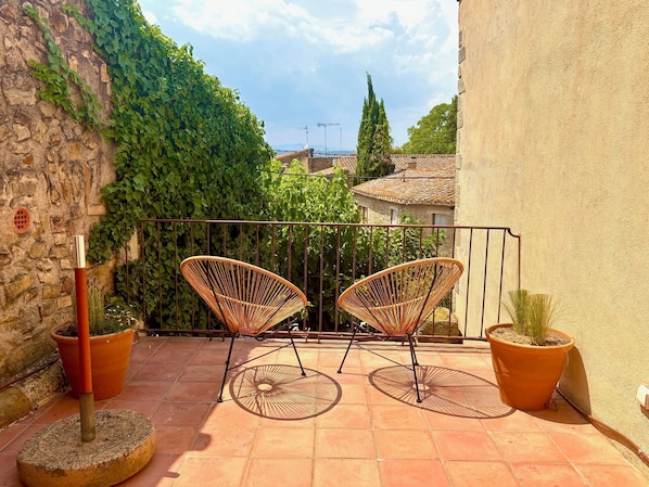 A balcony with two wicker chairs, potted plants, and a stone wall.