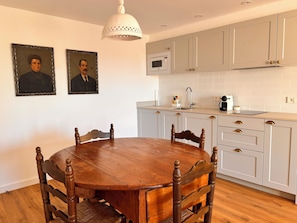 A kitchen with a round wooden table, white cabinets, a microwave, and two framed portraits on the wall.