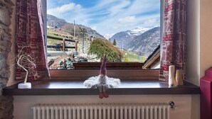 A window with a view of a mountain landscape, a gnome decoration, and a radiator. - Chez Margot et Sophie – Charm, Stonework and Alpine Views (Torgnon)