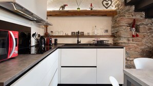 A modern kitchen with a stone wall, a red microwave, and a white dining area. - Chez Margot et Sophie – Charm, Stonework and Alpine Views (Torgnon)