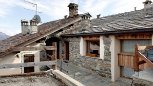 A stone building with a sloped roof, wooden stairs, and a wooden fence. - Chez Margot et Sophie – Charm, Stonework and Alpine Views (Torgnon)
