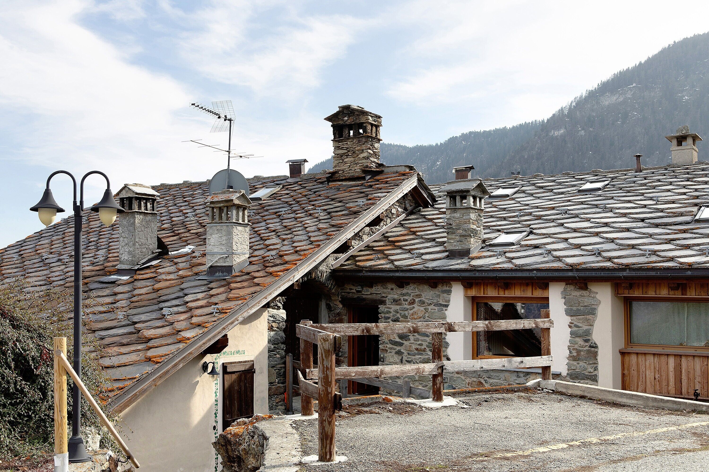 A traditional stone building with a sloped roof, wooden balcony, and a stone chimney.