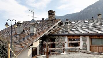 A traditional stone building with a sloped roof, wooden balcony, and a stone chimney.