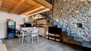 A modern kitchen with a stone wall, wooden ceiling, and a TV. - Chez Margot et Sophie – Charm, Stonework and Alpine Views (Torgnon)