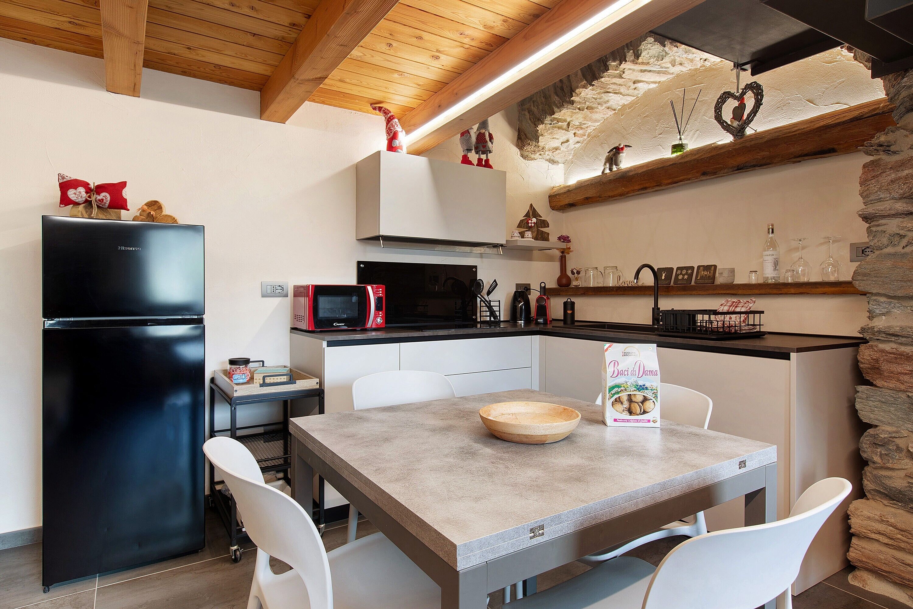 A kitchen with a black refrigerator, white chairs, a wooden table, and a stone wall.