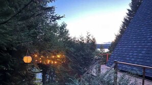 Un chemin menant à une maison au toit en pente, entourée d’arbres denses et agrémentée d’une lanterne suspendue.