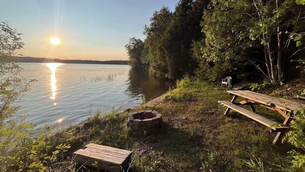 Un endroit au bord du lac, avec une table de pique-nique, un foyer et une chaise.