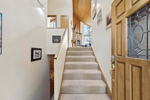 A staircase leading to a living area with a fireplace, framed pictures on the walls, and a wooden door with a glass panel.