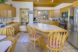 A kitchen with wooden cabinets, a large island with chairs, a refrigerator, and a stove.
