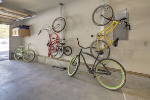 En garage med fire cykler lænet op ad væggen, en beton gulv og et træskab med genstande ovenpå.