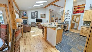 A spacious living area with a fireplace, a television, and a kitchen with a bar. - Verdin 6 - Lovely Lodge Style home, A/C, Private Hot Tub (Sunriver)