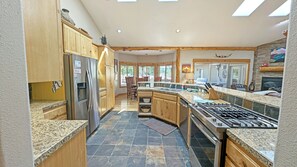 A spacious kitchen with granite countertops, wooden cabinets, a stainless steel refrigerator, and a gas stove.