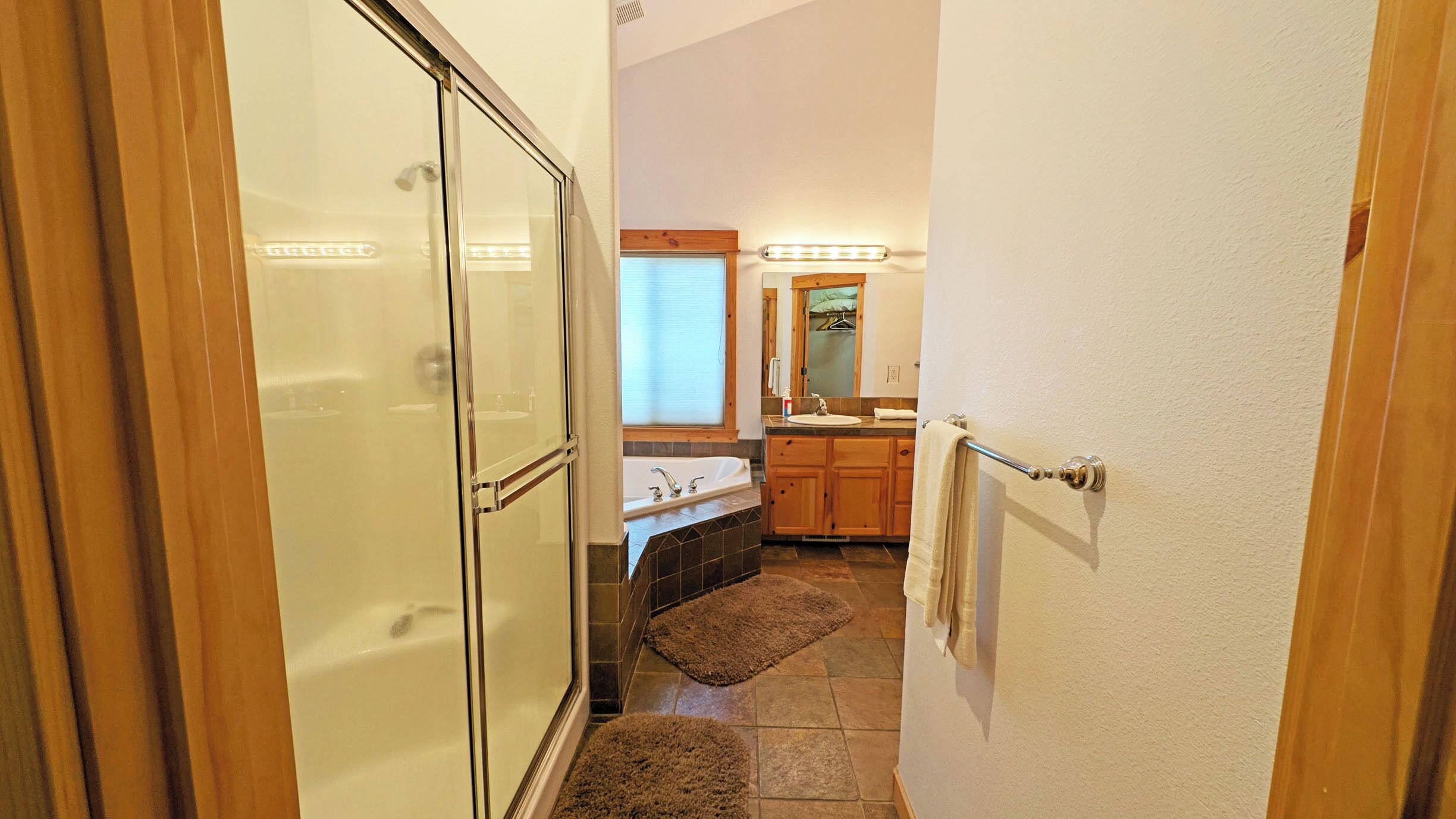 A bathroom with a glass shower enclosure, a sink with a mirror above it, and wooden cabinets.