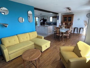 A living room with a yellow sofa, a round wooden coffee table, and a dining area with wooden chairs and a glass table.