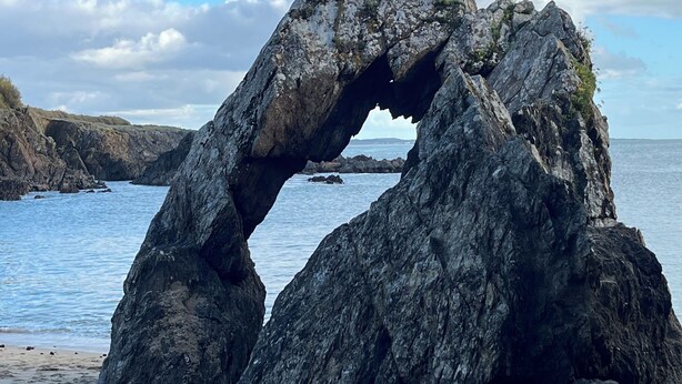 A natural rock formation with a hole in the middle, overlooking a beach and the sea.