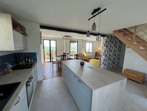 A modern kitchen with a central island, dining area with chairs, and a view to the outside.